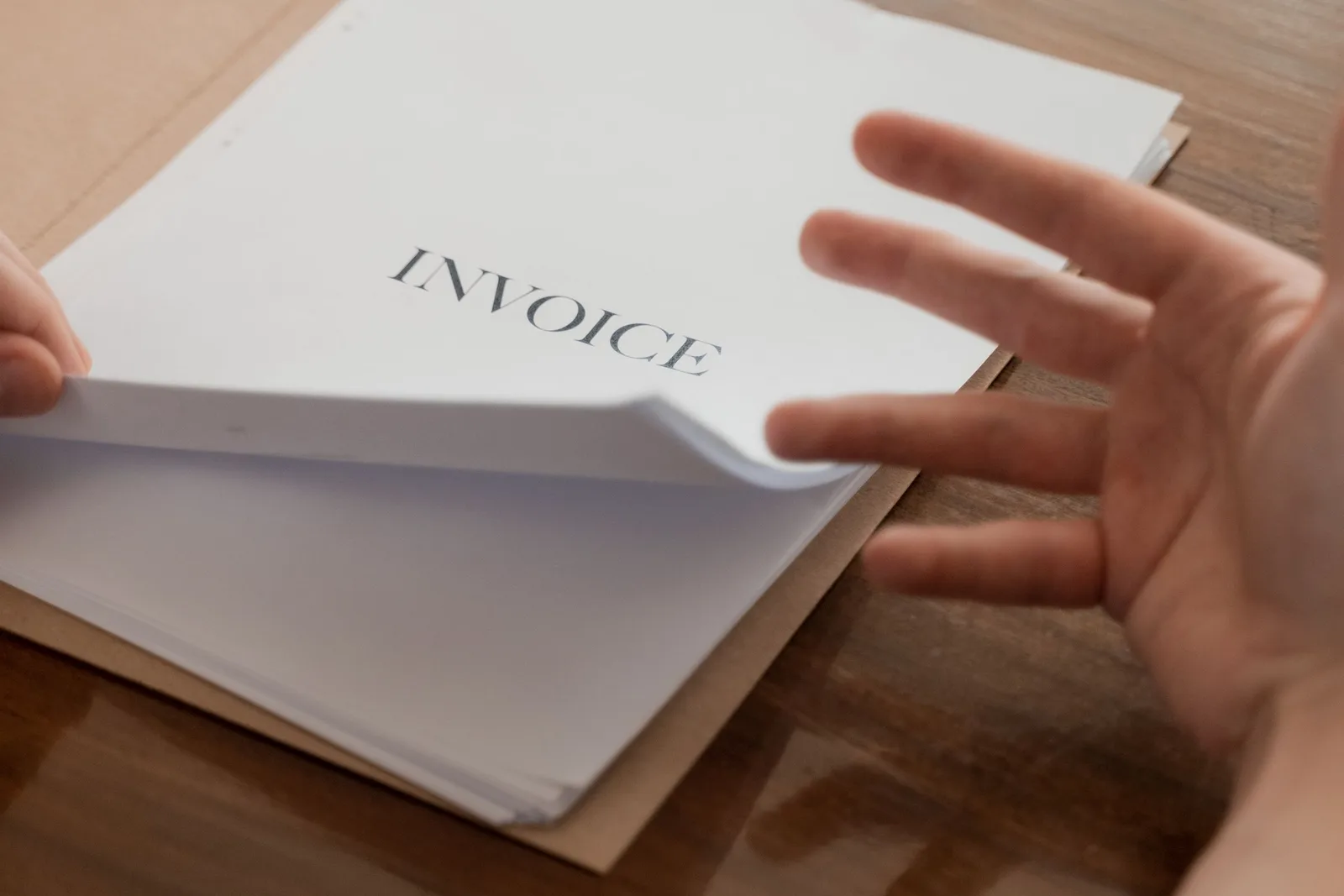 Üzerinde INVOICE yazan bir dosyayı açan el