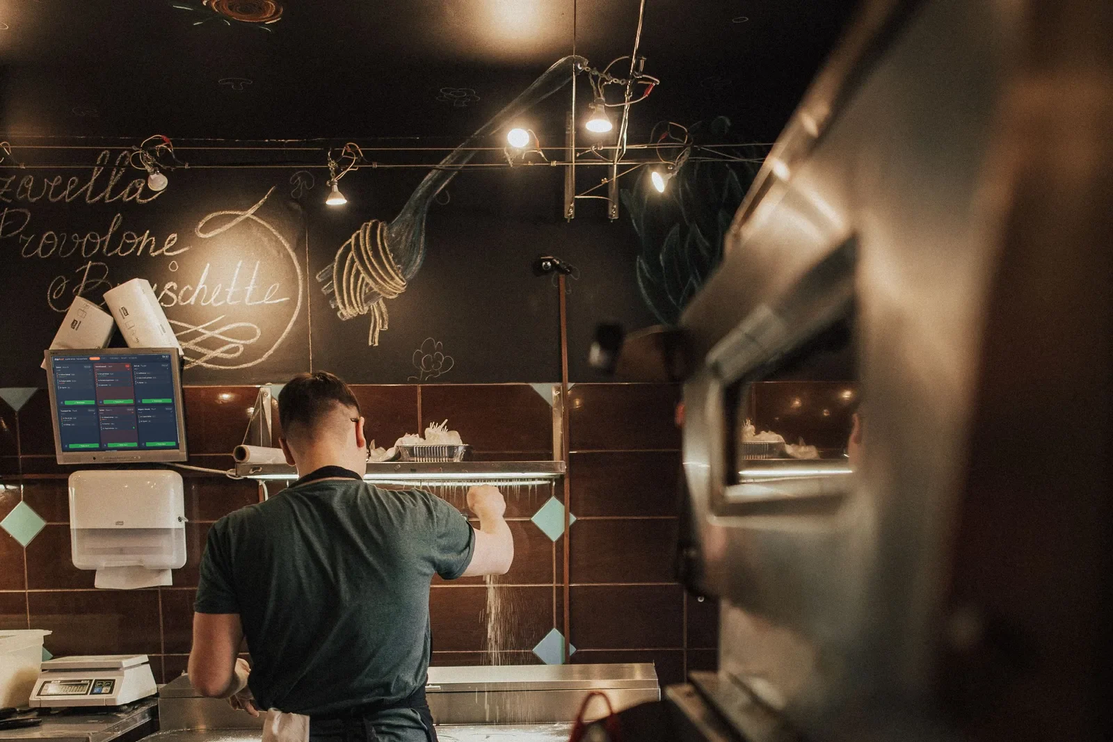 A kitchen display mounted on the wall above the line, with a cook working the counter