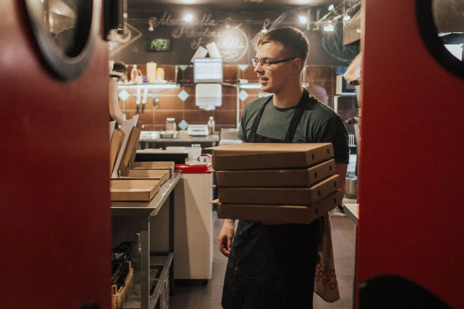 Restaurant worker carrying a stack of boxed delivery orders past the pass